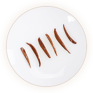 Six slender copper-brown infused tea buds on a white dish
